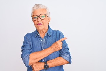 Senior grey-haired woman wearing denim shirt and glasses over isolated white background Pointing with hand finger to the side showing advertisement, serious and calm face