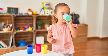 Beautiful blond toddler girl drinking glass of water at kindergarten