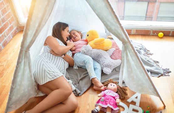 Beautiful teacher and blond toddler girl lying down on the floor inside tipi at kindergarten