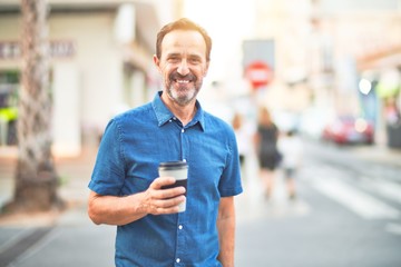Middle age handsome man standing on the street drinking take away coffee smiling