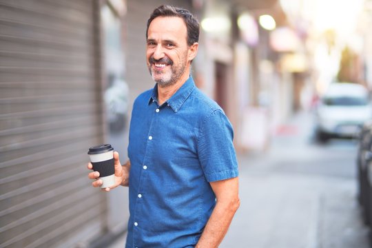 Middle age handsome man standing on the street drinking take away coffee smiling