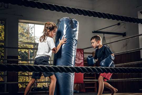 Dark photo shoot of kids training with big punching bag at boxing studio.