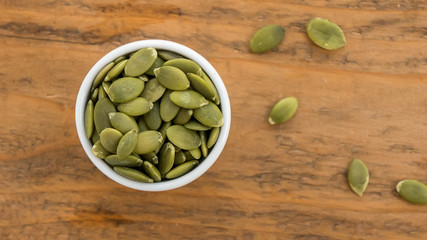 Pumpkin seeds in white bowl over wooden background top view