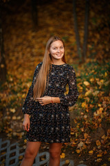 a girl in a black floral dress on a background of fallen leaves, taken on an autumn evening