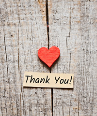 Thank You text on a small piece of paper. Wooden background and a small heart.
