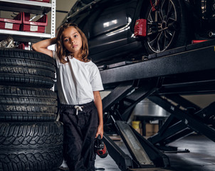 Little cute child is posing for photographer handing pneumatic drill at car's workshop.