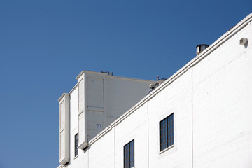 Upward view of a section of an old white warehouse under a deep blue sky