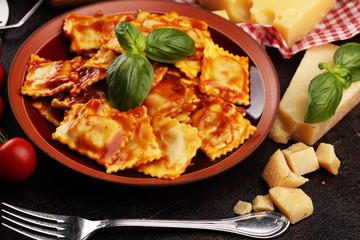 Ravioli with tomato sauce garnished with parmesan cheese and basil on rustic table