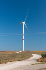 Wind turbines in the field. Country road past a windmill turbine, close up. Huge wind generators in countryside against blue sky