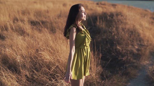 Beautiful woman stands in field at sunset and breathes deeply, slow motion