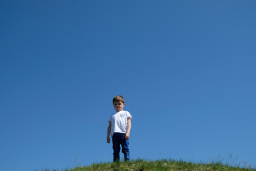 Trauriger, einsamer Junge auf einer Bergkuppe mit blauem Himmerl im Hintergrund