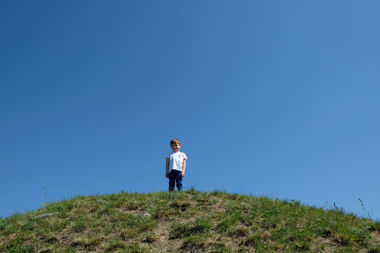 Trauriger, einsamer Junge auf einer Bergkuppe mit blauem Himmerl im Hintergrund