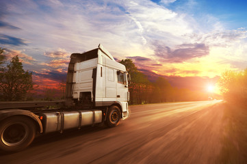 A big truck driving fast on the countryside road against a sky with sunset