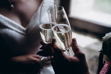 Horizontal image of a married couple toasting champagne glasses at wedding party. Hands bride and groom clinking glasses at wedding reception.