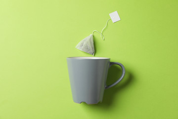 Cup and tea bag on green background, copy space