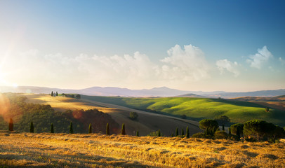sunset over autumn Tuscany countryside landscape; rolling hills and village
