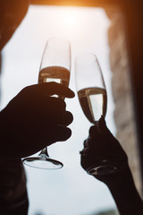 Close up of silhouette married couple toasting champagne glasses at wedding party. Hands bride and groom clinking glasses at wedding reception.