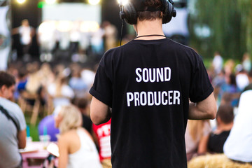 Technician guy in headphones and t-shirt with the inscription sound producer on his back at a outdoor show