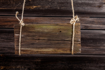 An old wooden bulletin board hangs on a string against a wooden wall