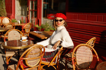 Young beautiful elegant woman in French style cafe wearing in white sweater and red beret and...