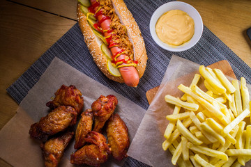 Assorted fast food closeup top view: hot dog, french fries, grilled wings and cheese sauce.