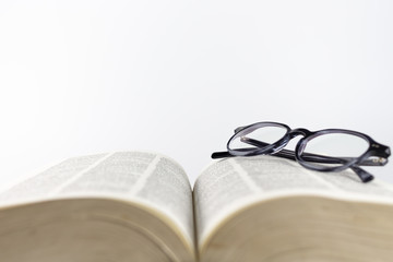 Close-up of a folded reading glasses on an open book on a white background