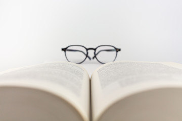 Close-up of an open book with reading glasses on a white background