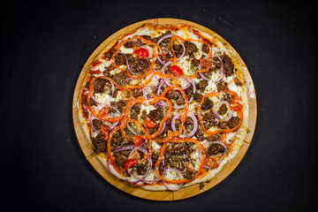 Pizza bolognese cooked on thin pastry top view close-up on a black background.