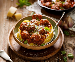 Meatballs in tomato sauce with Pappardelle pasta sprinkled with grated parmesan cheese and chopped basil in a ceramic dish on a wooden rustic table