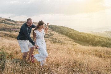 Young couple man and woman in love walking on the field on the mountain in autumn or summer day hugging together having fun bonding flirting flirt husband and wife lovers