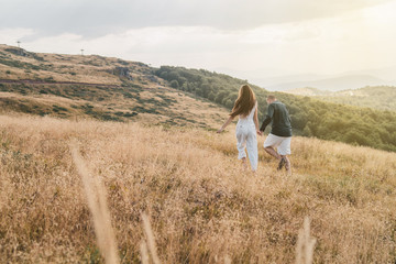 Fototapeta na wymiar Young couple man and woman in love walking on the field on the mountain in autumn or summer day hugging together having fun bonding flirting flirt husband and wife lovers