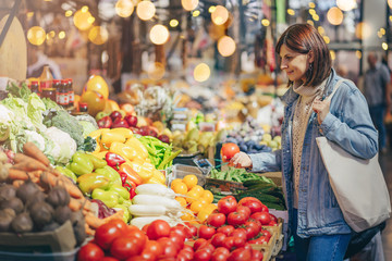 Woman is chooses fruits and vegetables at food market. Reusable eco bag for shopping. Sustainable...