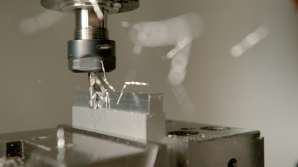MACRO: Sharp industrial drill spinning and end milling a piece of aluminium.