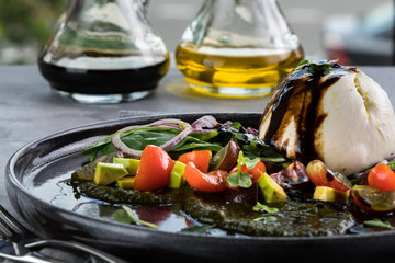 Burrata fresh italian cheese with Sauce pesto and vegetables. Bottles with sauce, gray tablecloth, spoon and fork. Opposite the large window in the restaurant
