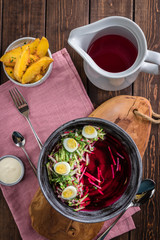 Cold beetroot soup with eggs, baked potatoes, souce, rustic wooden background, white jug, pink tablecloth, top view