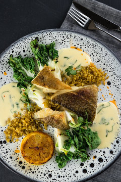 Spotted wolffish fillet with spicy bulgur and fried Pak-choi and lemon. Top view