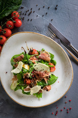 Salad with burrata, parma and cherry tomatoes confit. Spoon and a fork on the grey background