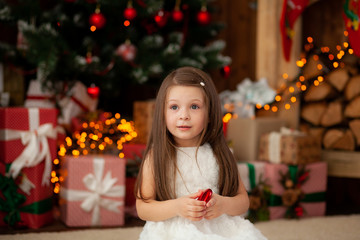 Happy pretty girl 4-5 playing with a toy railway in front of a Christmas tree with Christmas presents. New Year holiday.