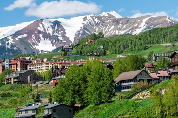Fototapeta na wymiar Mount Crested Butte snow marooon color mountain in summer with green lush color on hills slopes and houses cityscape