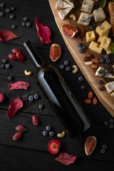 A bottle of red or white wine in dark glass on black boards with a snack of cheese, nuts and berries