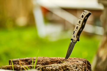 Folding knife on a stump on a background of grass