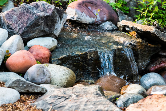 Small water fountain waterfall closeup in garden park with rock pond and colorful multicolored stones in Colorado
