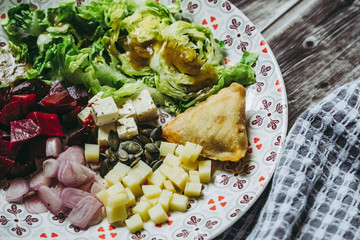 Assiette de salade composée avec dés de fromage betteraves échalotes graines de courge samoussa	