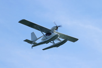 Floatplane (seaplane or hydroplane) flying in blue sky closeup. Cabin, wings propeller, engine, tail of plane are visible in details.
