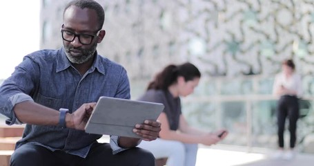 Businessman working on digital tablet and smartwatch on office rooftop terrace - Powered by Adobe