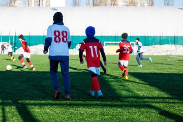 Boys in white and red sportswear plays  football on field, dribbles ball. Young soccer players with ball on green grass. Training, football, active lifestyle for kids , winter sport