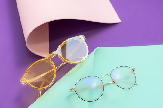 Reading glasses on violet, neo mint, coral color paper rolls, copy space. Trendy lay out flat lay with glassware. Astigmatism correction concept, shine  lenses. Vision care, glasses for work on pc
