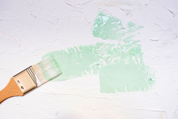 Brush with wooden handle with gentle breeze paint on white putty textured background. Neo mint...