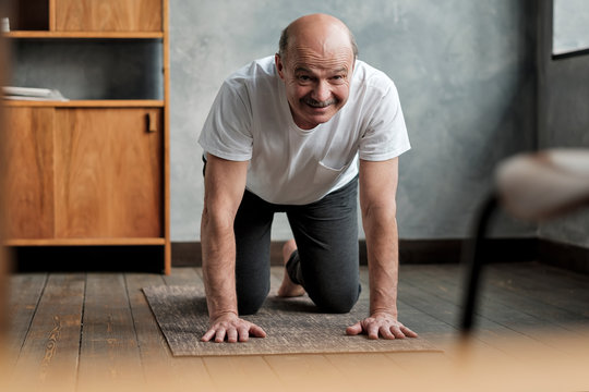 Senior hispanic man practices yoga asana marjariasana or cat-cow pose at home. Doing sport exercise for spine health.