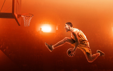 Professional basketball player on basketball court in action with the ball. Slam Dunk. Red floodlit...